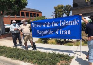 Ali and comrades hold a blue banner that says "Down with the Islamic Republic of Iran."