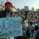 A farmer holds a sign saying "No Farmer, No Food: Shame On Modi" in front of a crowd of other protesting farmers
