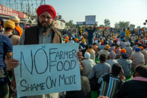 A farmer holds a sign saying "No Farmer, No Food: Shame On Modi" in front of a crowd of other protesting farmers